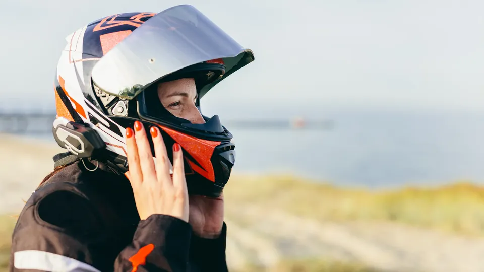 Person i motocykel-hjelm justerer nakkebeskytter udendørs.