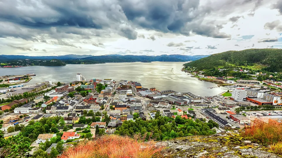 Luftfoto av Namsos sentrum langs fjorden med havn og omliggende skogkledde fjell.