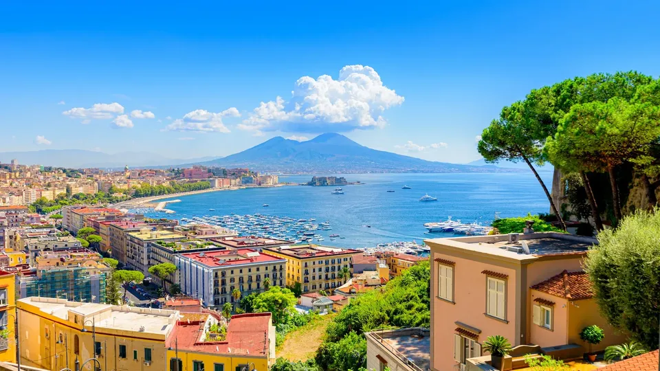 Città costiera che si affaccia sulla baia con vulcano in lontananza.