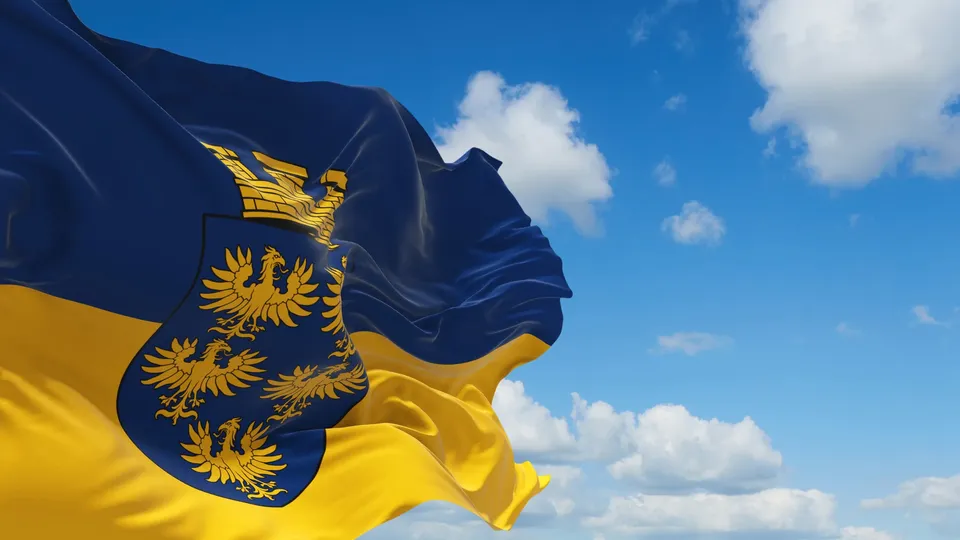 Blau-gelbe Flagge Niederösterreichs mit dem niederösterreichischen Wappen vor blauem Himmel mit Wolken.