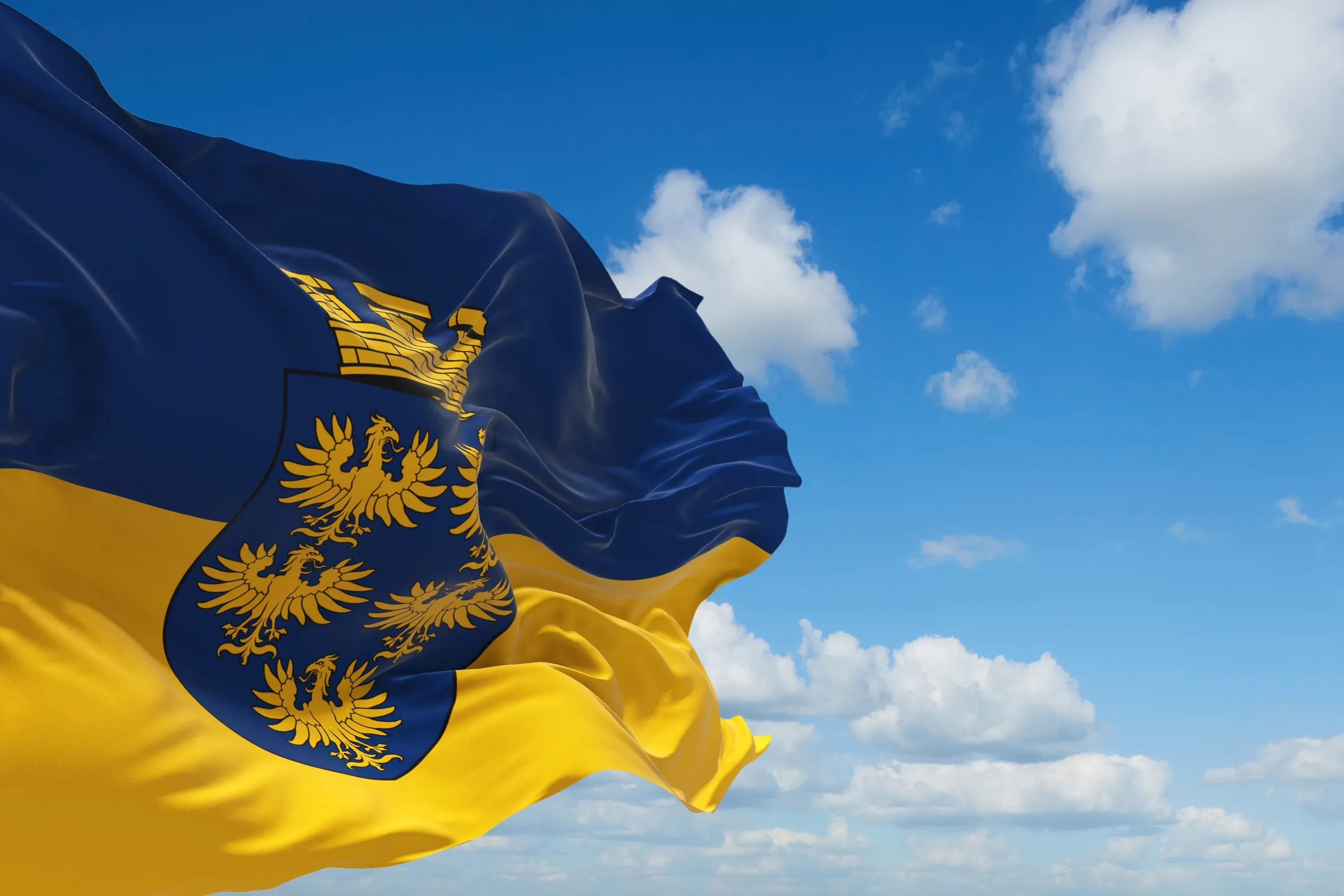 Blau-gelbe Flagge Niederösterreichs mit dem niederösterreichischen Wappen vor blauem Himmel mit Wolken.
