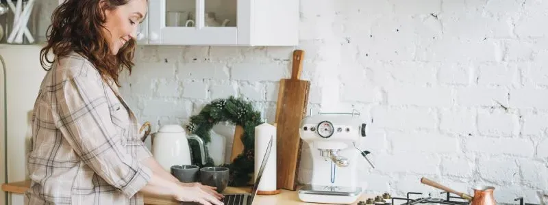 Smilende kvinde i et køkken, der kigger efter en ny elaftale på sin computer.