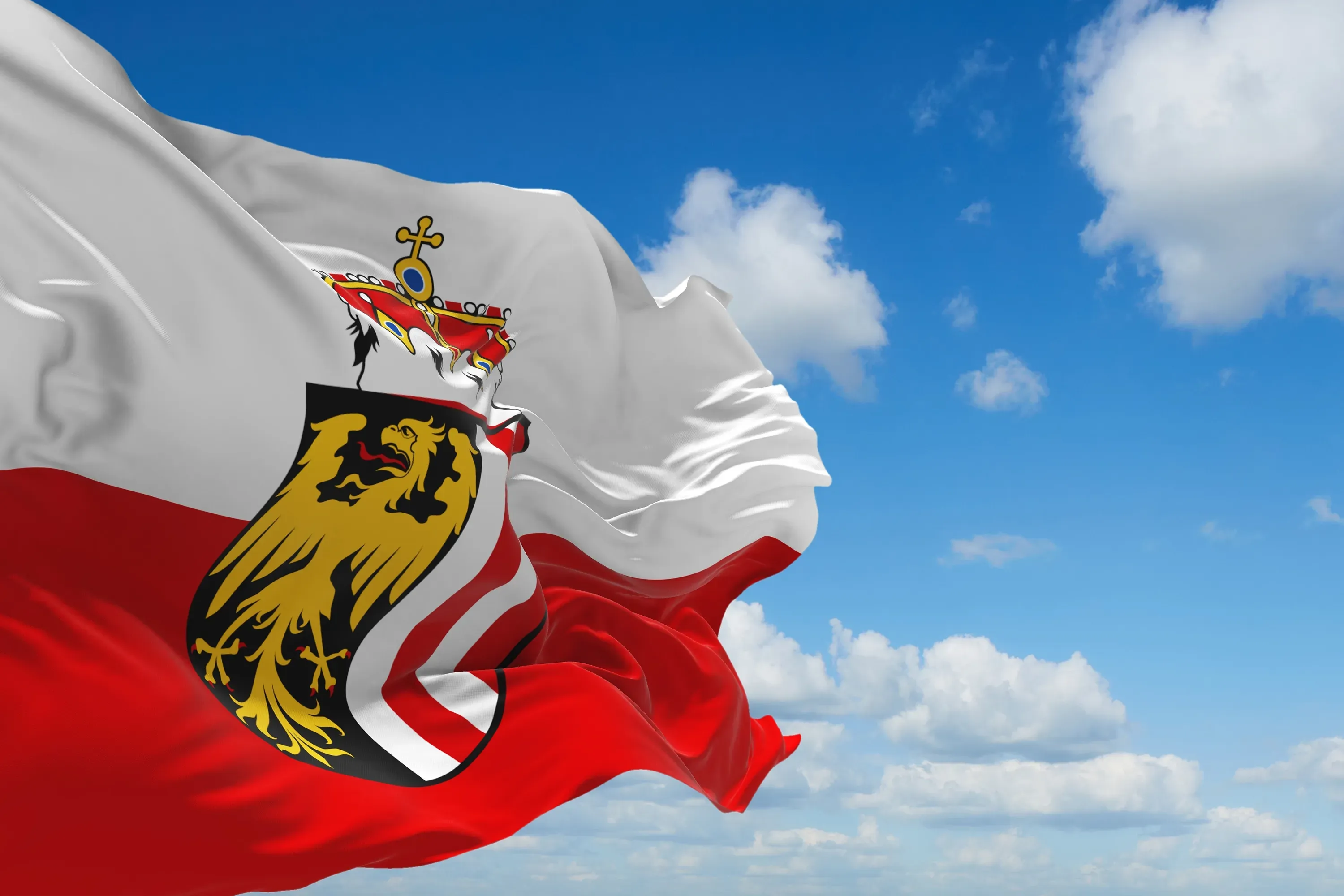 Rot-weiße Flagge Oberösterreichs mit dem oberösterreichischen Wappen vor blauem Himmel mit Wolken.