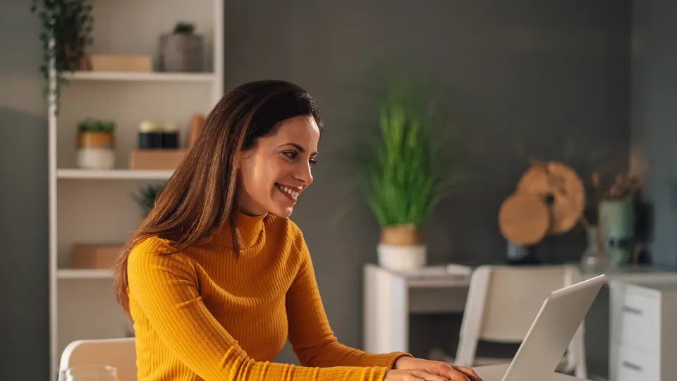 Mujer sonriendo mientras escribe en su laptop en el escritorio.