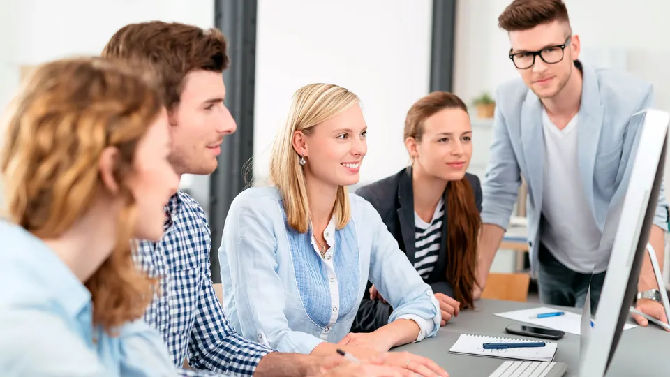 Equipo de cinco personas reunidas alrededor de un monitor de computadora en una oficina.