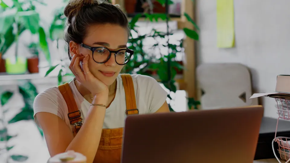 Mujer con gafas trabajando en laptop en escritorio.