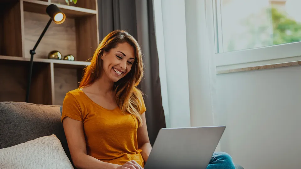 Mujer sonriendo mientras usa laptop en el sofá.
