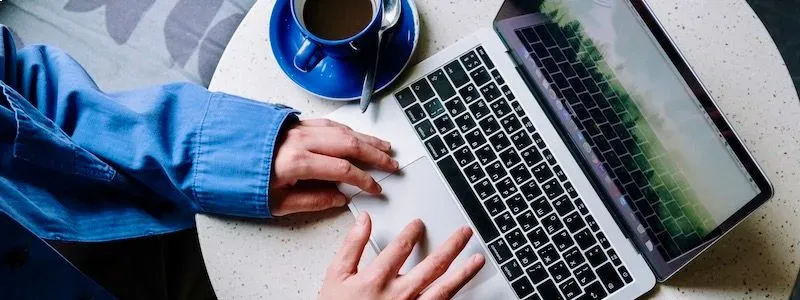 Hænder på en computer med en kaffekop ved siden af.