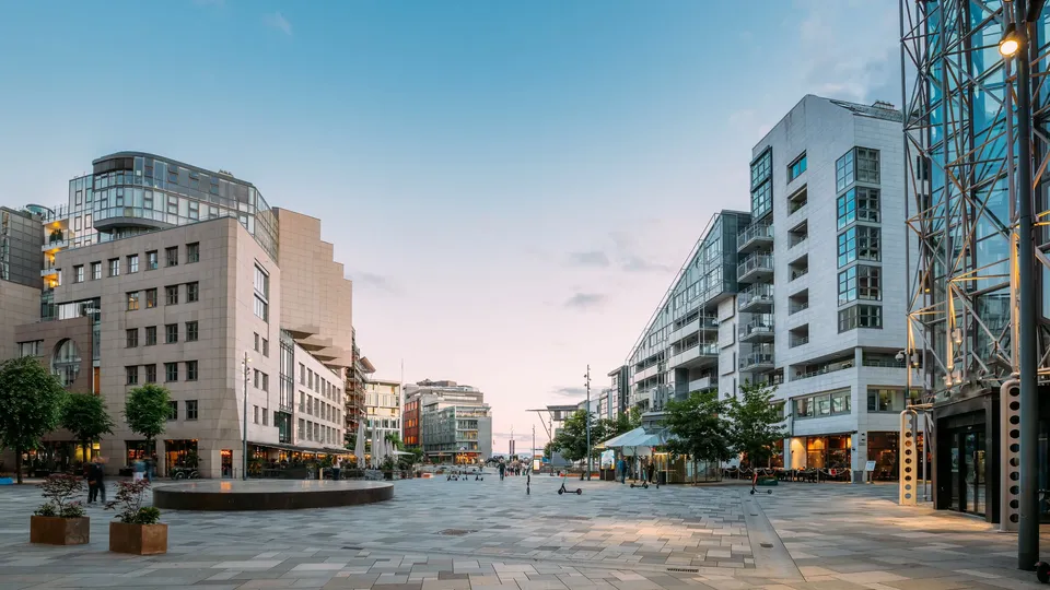 Tom brolagt plass mellom moderne leilighetsbygg ved skumring.