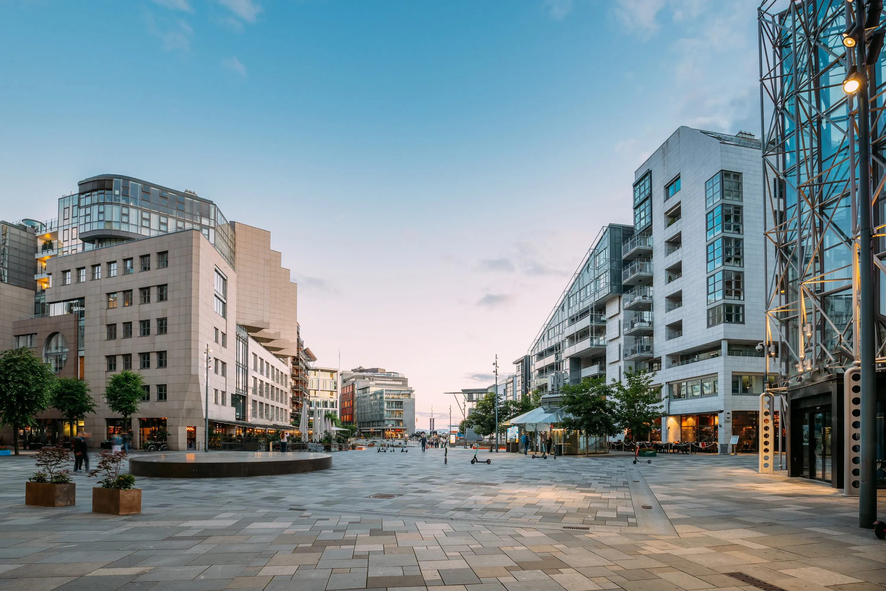 Tom brolagt plass mellom moderne leilighetsbygg ved skumring.