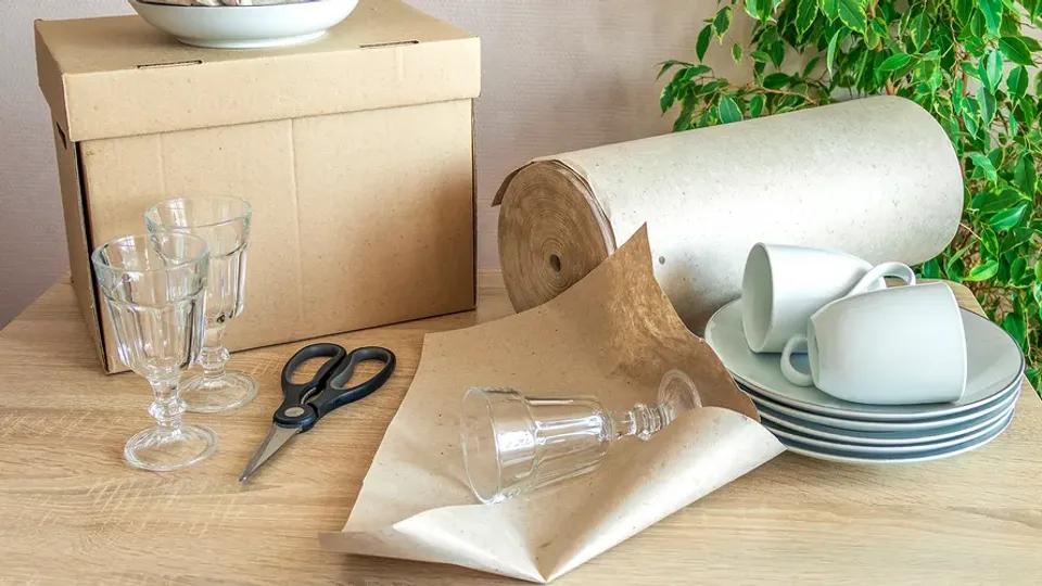 Glas, porslin och packmaterial står förberett för flyttpackning på ett bord.