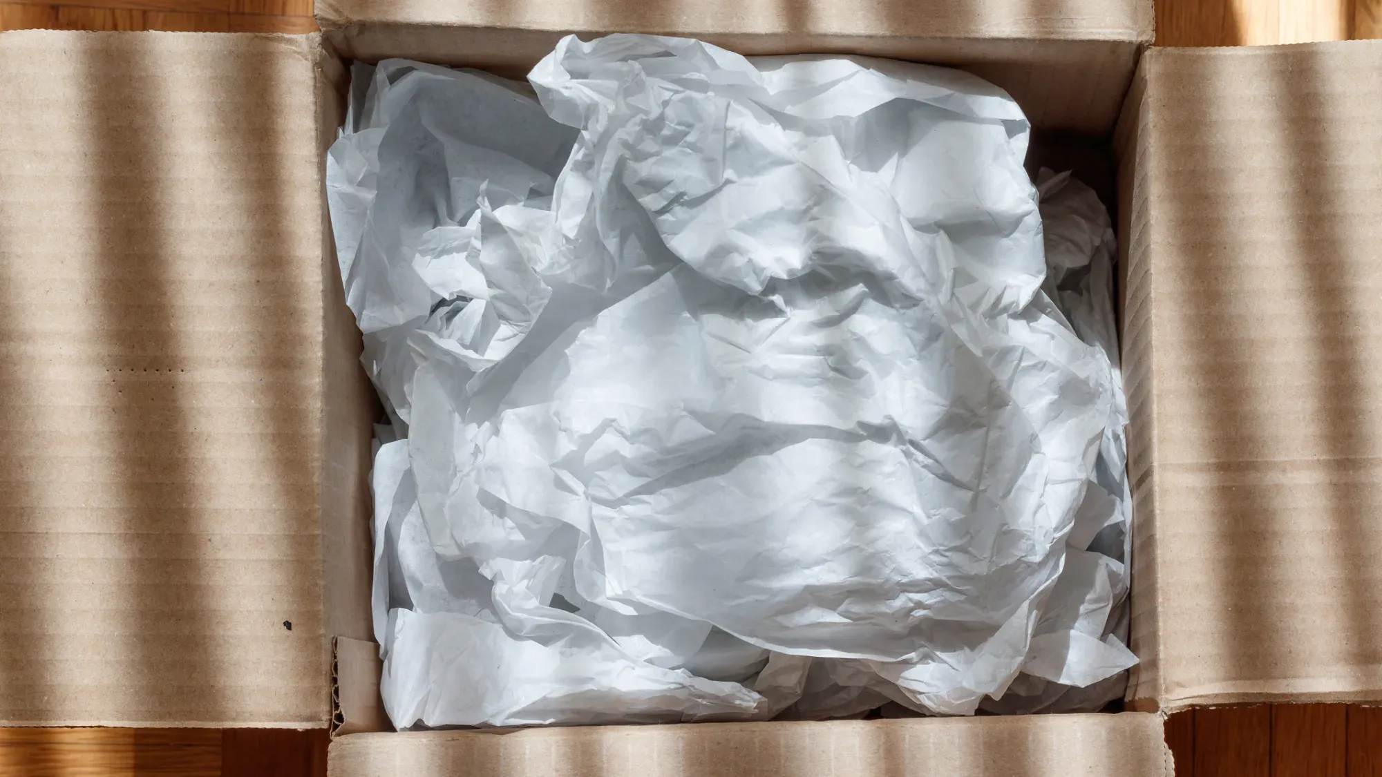 Flyttkartong med knycklat silkespapper i botten som stötdämpning vid packning av glas.