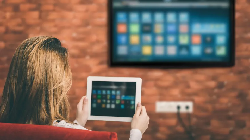 Kvinde holder tablet mens hun ser på TV med farverig app-gitter.