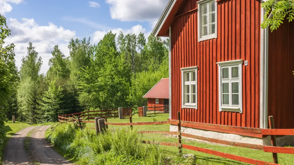 Rött trähus med vita fönster och inhägnat område omgivet av skog.