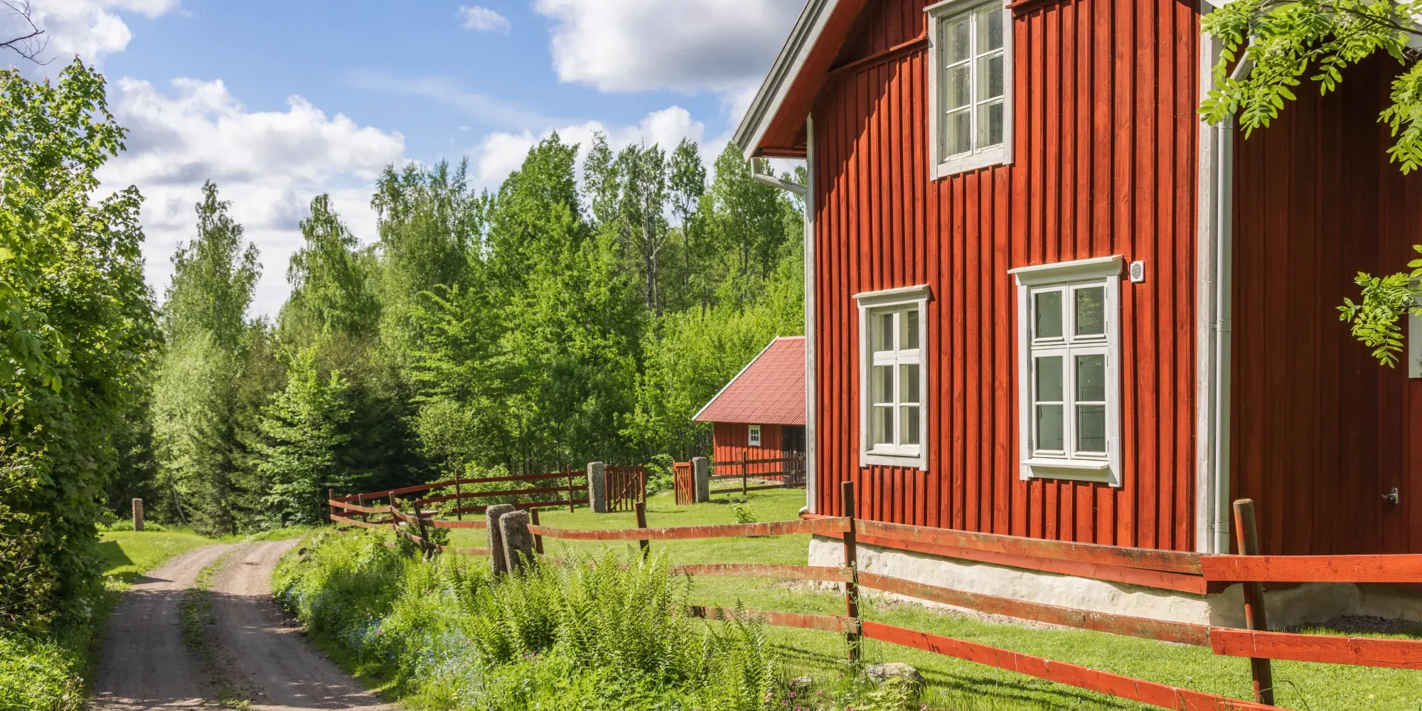 Rött trähus med vita fönster och inhägnat område omgivet av skog.