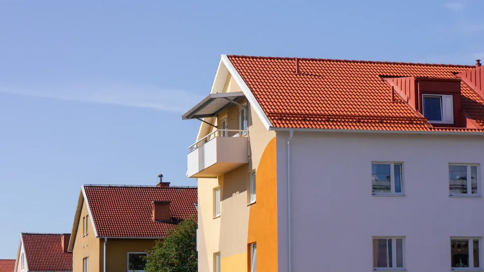 Färgglada bostadshus med röda takpannor och moderna balkonger mot blå himmel.