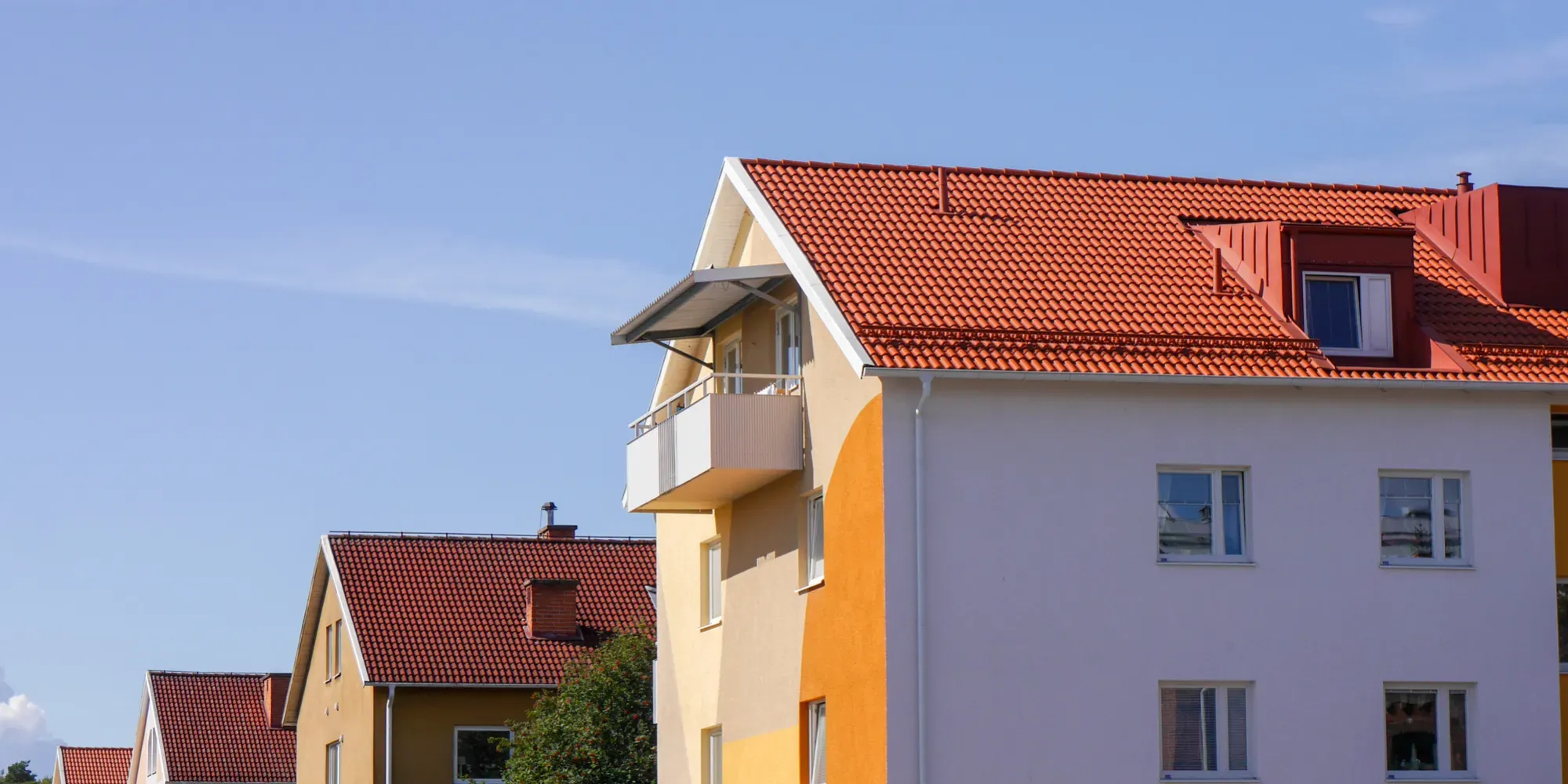 Färgglada bostadshus med röda takpannor och moderna balkonger mot blå himmel.