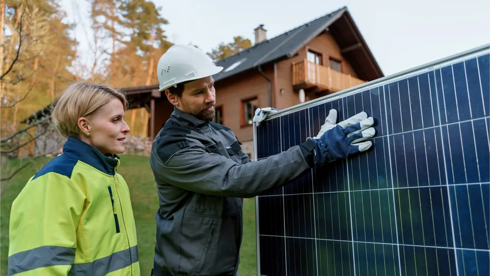 Zwei Arbeiter begutachten ein Photovoltaikmodul vor einem Wohnhaus.