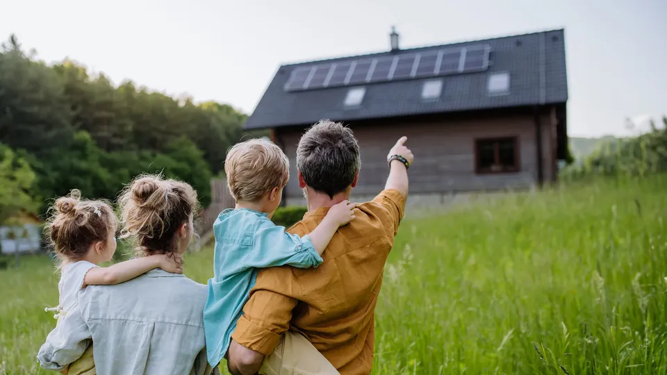 Vierköpfige Familie blickt auf ein Haus mit Photovoltaikanlage auf dem Dach.