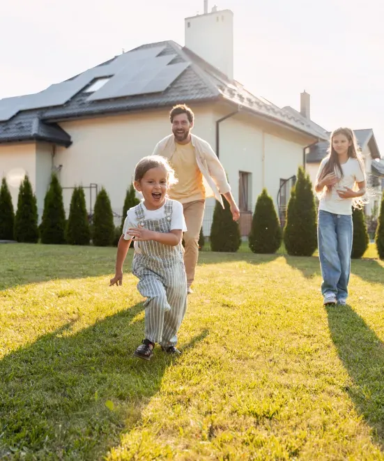 Famiglia corre nel giardino di casa con pannelli solari sul tetto.