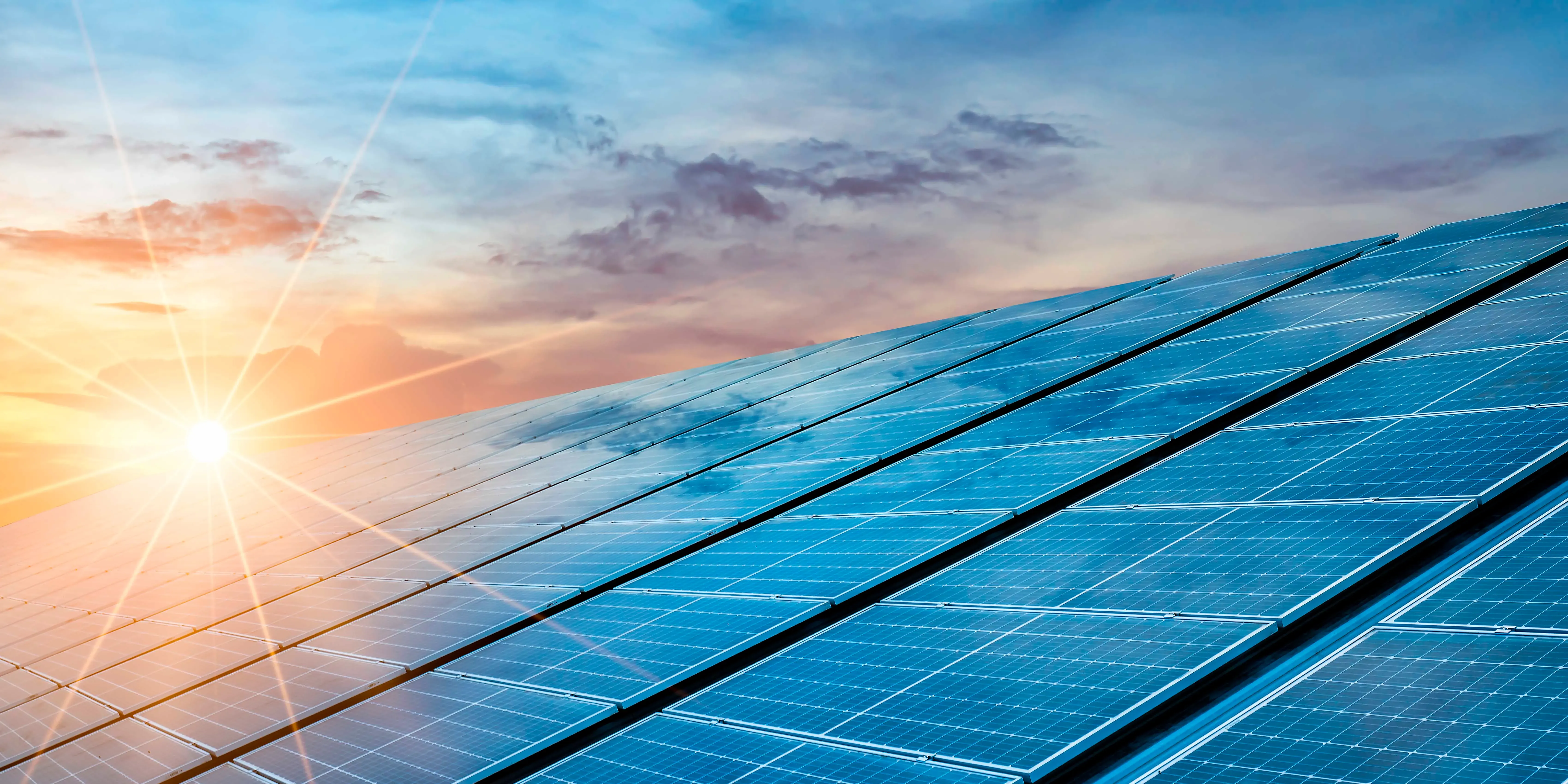 Paneles solares inclinados hacia la puesta de sol con sol brillante y cielo nublado.