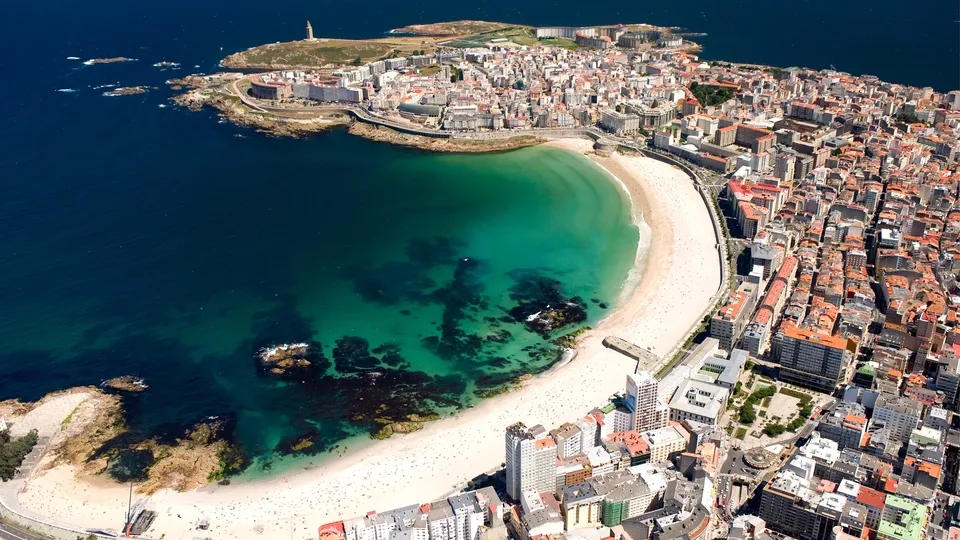 Vista aérea de ciudad costera con playa de arena curva y agua turquesa.