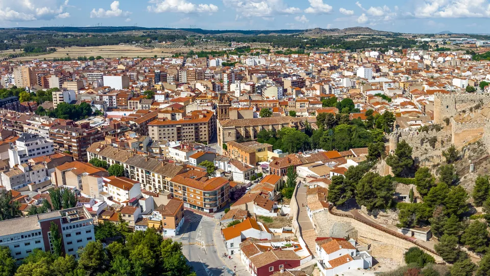 Vista aérea de una ciudad española con tejados de barro, ruinas de castillo en la ladera y campo circundante.