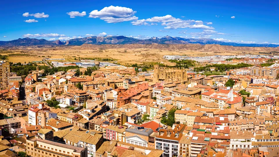 Vista aérea de una ciudad española con tejados de terracota y montañas al fondo.