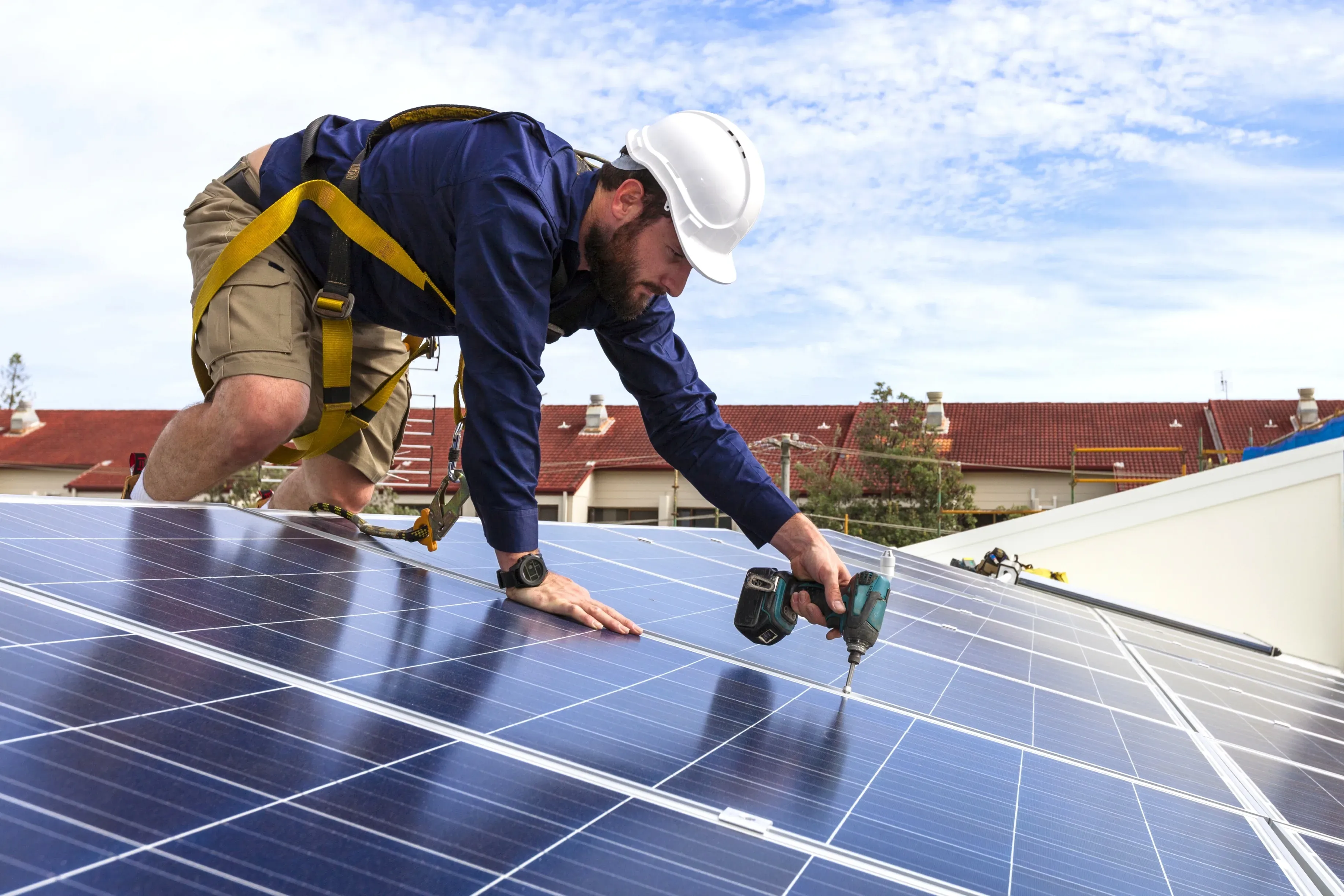Trabajador instalando panel solar en tejado con taladro.