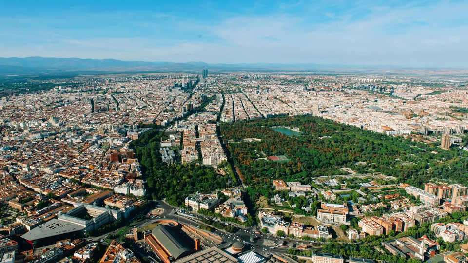 Vista aérea del paisaje urbano de Madrid con gran parque verde en el centro rodeado de edificios.