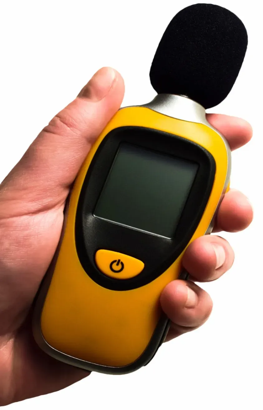 Mano sosteniendo medidor de nivel de sonido amarillo y negro con micrófono.