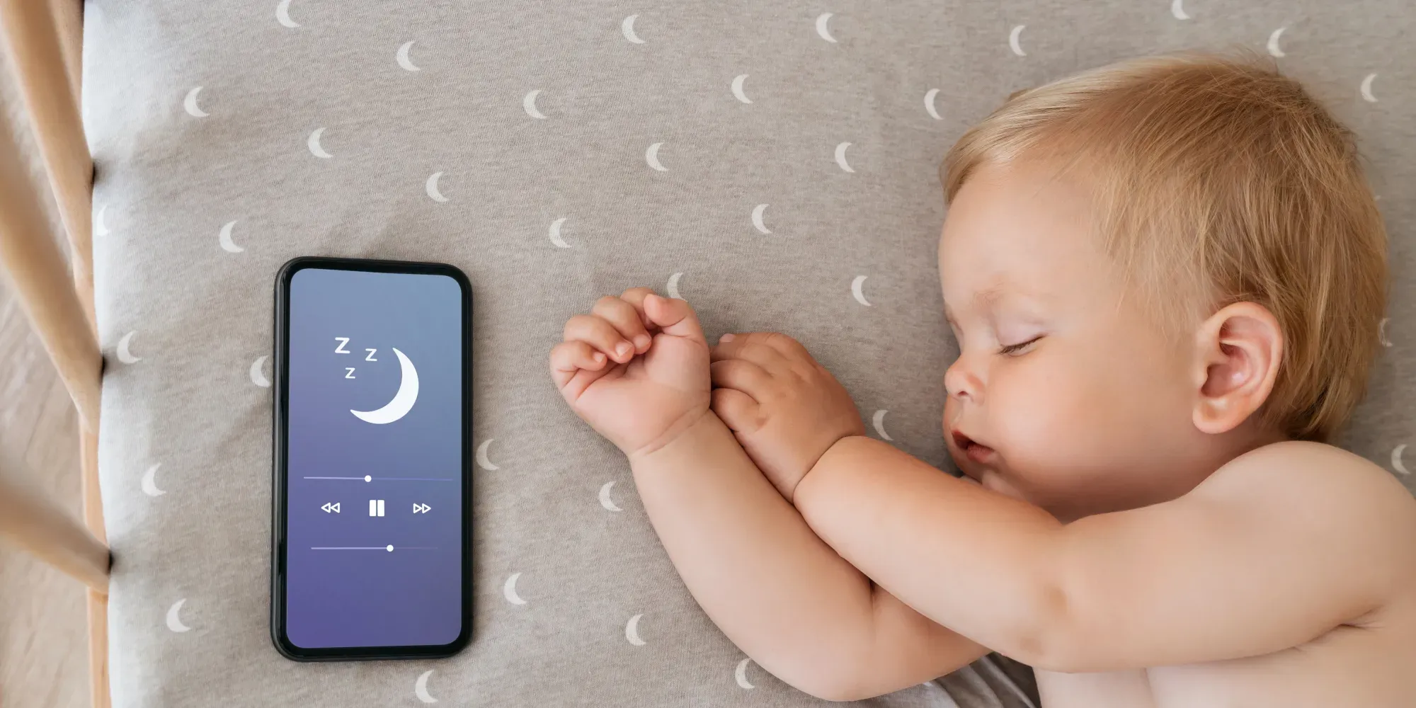 Bebé durmiendo junto a teléfono que muestra aplicación de sueño con icono de luna.
