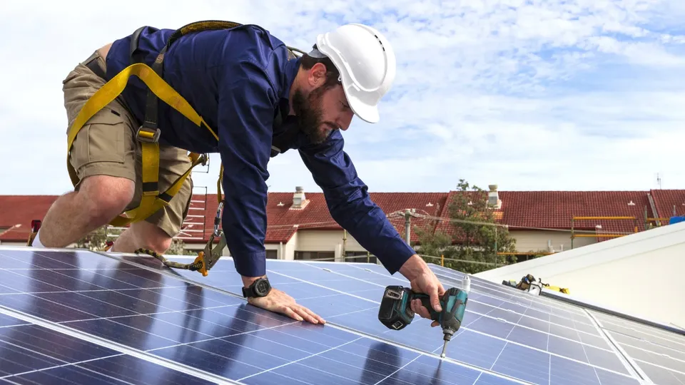 Trabajador instalando panel solar en tejado con taladro.