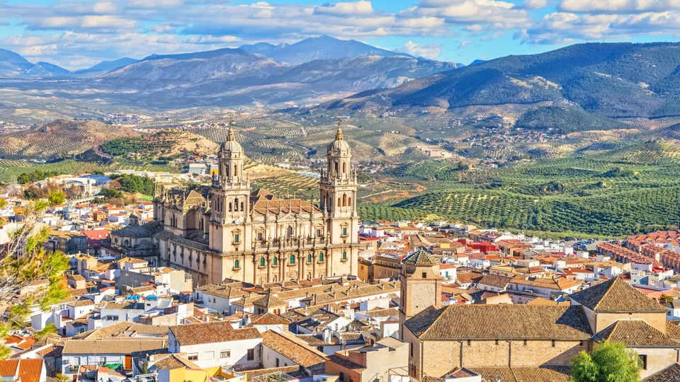 Catedral con torres gemelas dominando un pueblo y olivares en un valle montañoso.