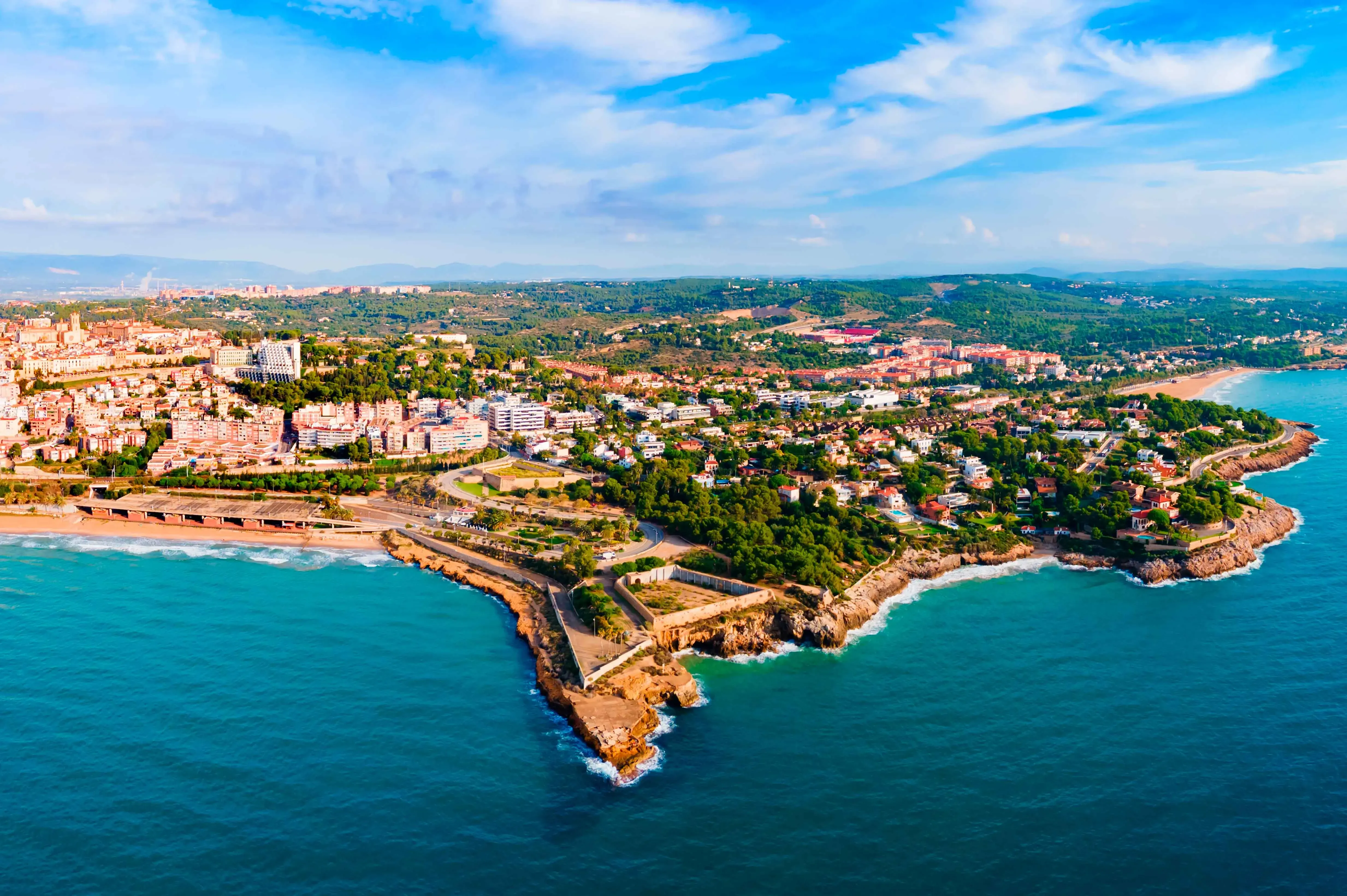 Vista aérea de ciudad costera con mar turquesa y península rocosa.
