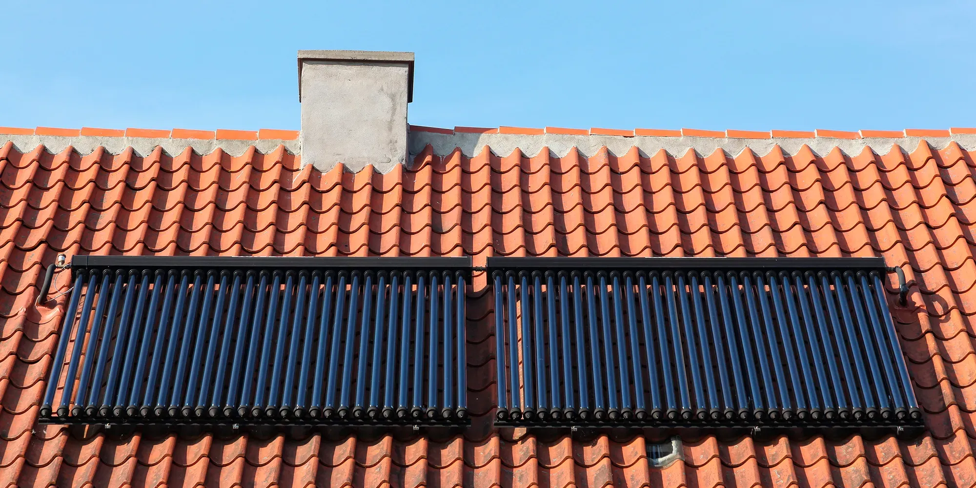 Dos paneles solares térmicos montados en un tejado de tejas de barro con chimenea.