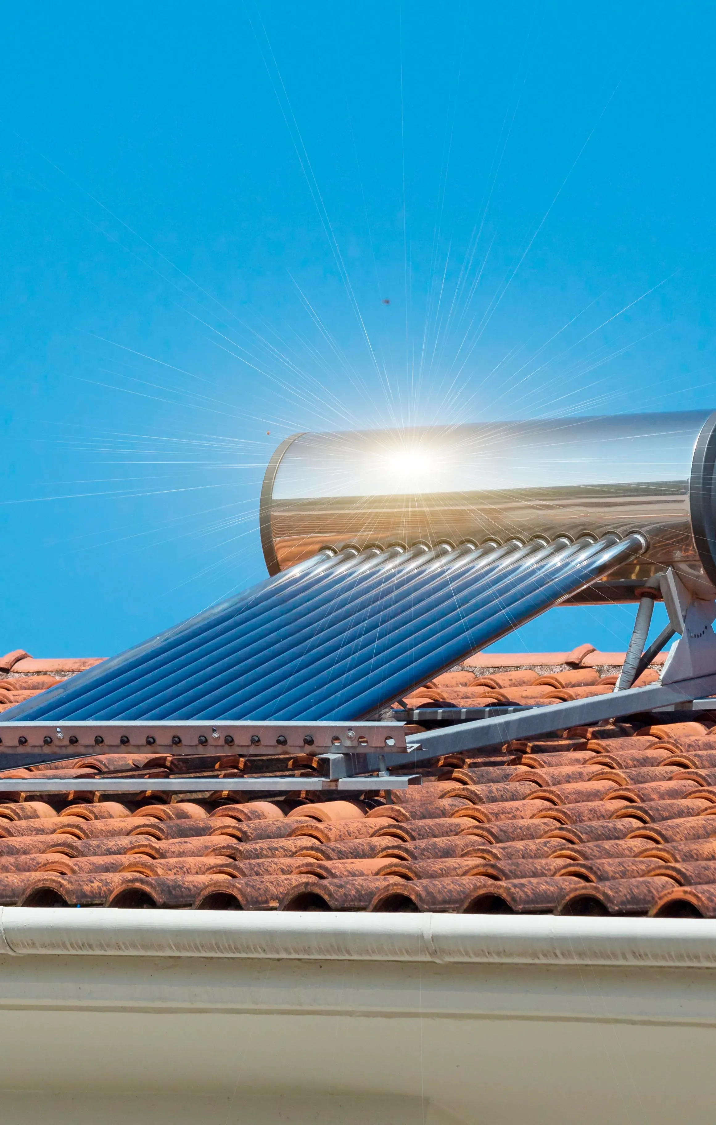 Colector solar térmico en tejado con luz solar reflejada en tubos metálicos.
