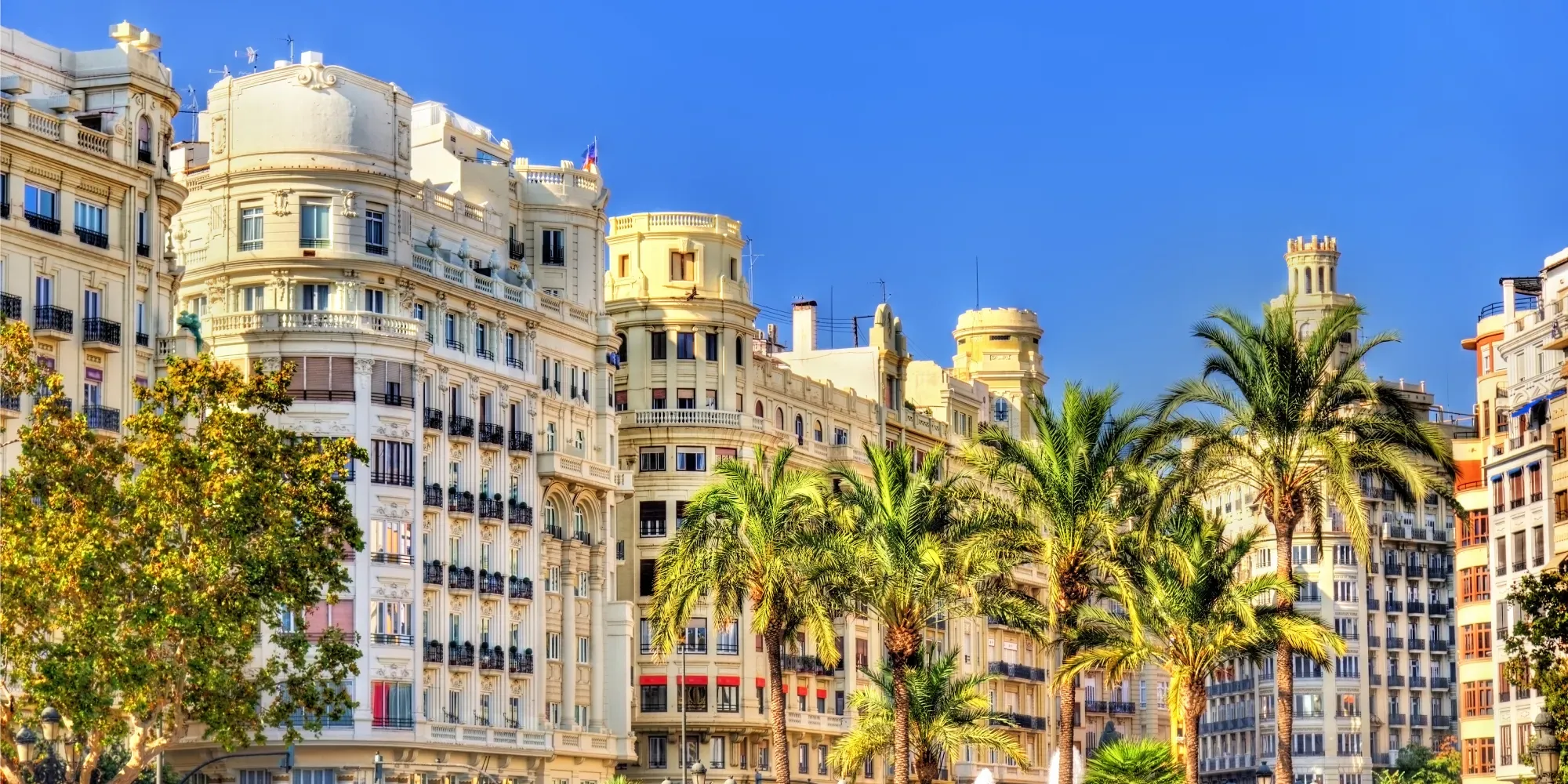 Edificios beige ornamentados con palmeras en una calle mediterránea.