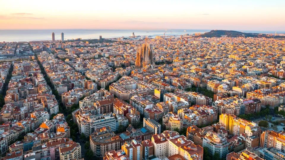 Vista aérea del paisaje urbano de Barcelona al atardecer con la catedral Sagrada Familia prominente en el centro.