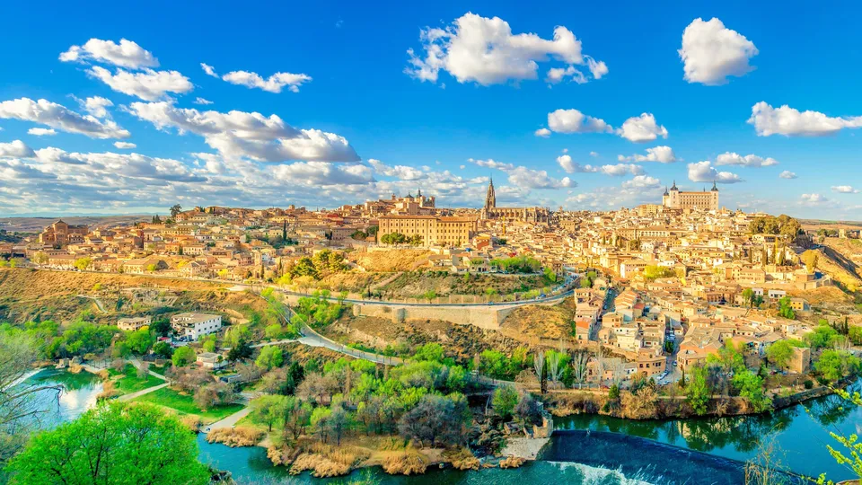 Ciudad histórica amurallada en colina rodeada de río y paisaje verde bajo cielo azul.