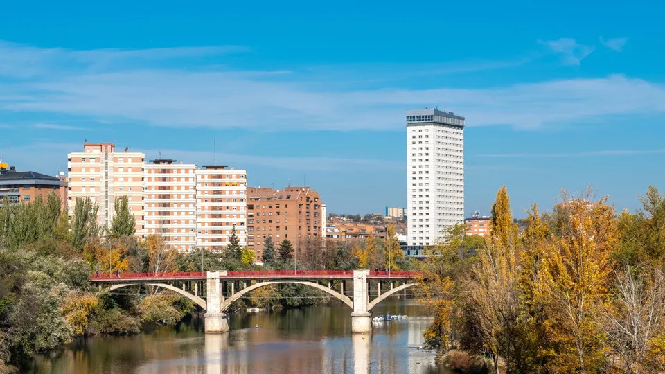Puente rojo sobre río con edificios de apartamentos y árboles en otoño.