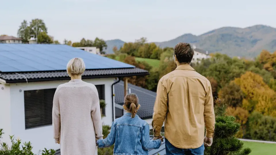 Family of three viewing a house with solar panels on the roof.