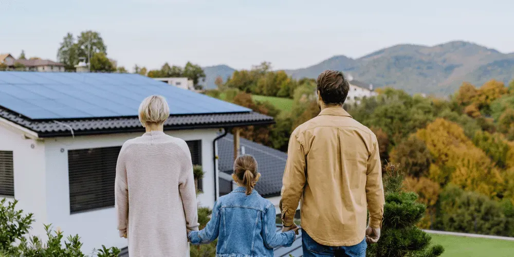 Family of three viewing a house with solar panels on the roof.