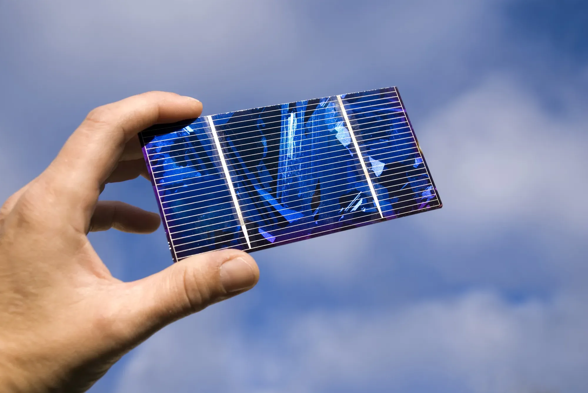 Hand hält ein kleines Solarpanel gegen blauen Himmel.