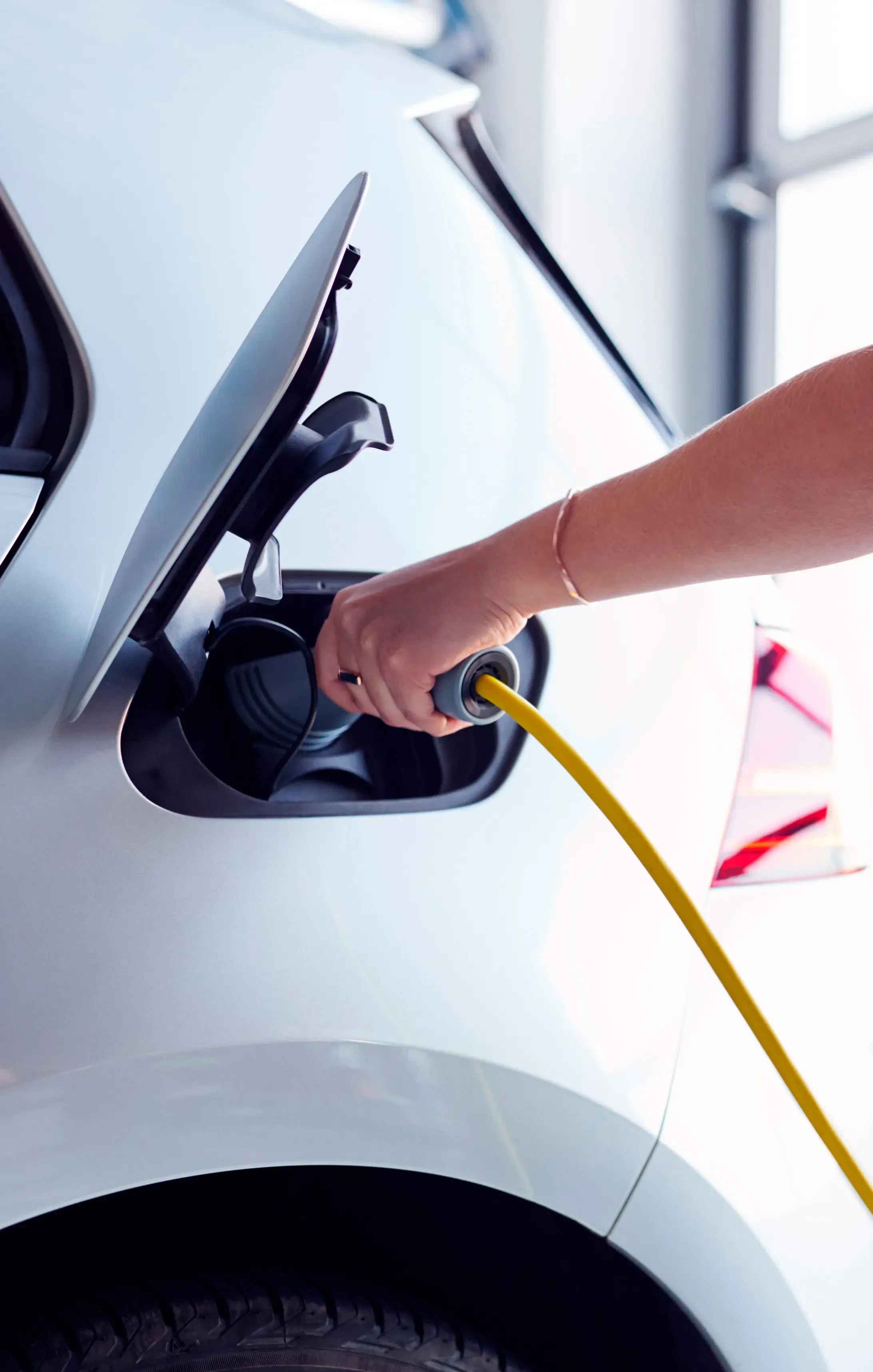 Hand plugging yellow charging cable into electric vehicle port.