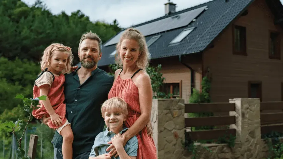 Family of four standing in front of house with solar panels on roof.