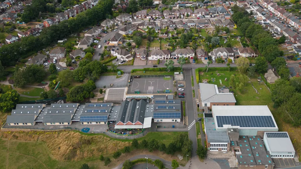 Aerial view of suburban neighborhood with schools, residential homes, and solar panels on rooftops.