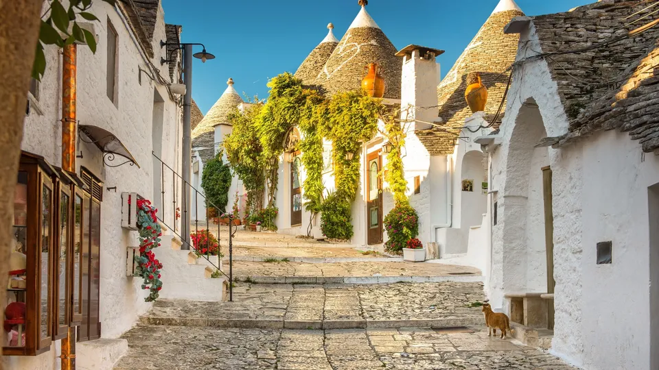 Affascinante strada in ciottolato fiancheggiata da case trulli con muri bianchi e tetti a forma di cono.