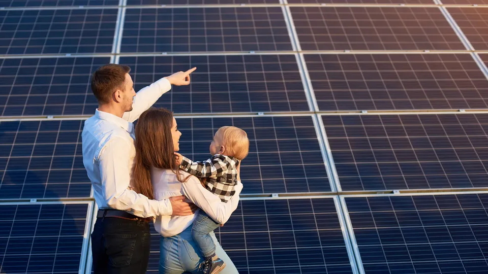 Familie mit kleinem Kind zeigt gemeinsam auf eine große Photovoltaikanlage.