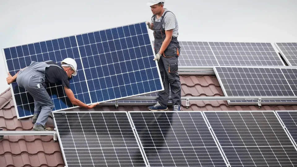 Two workers installing solar panels on a roof.